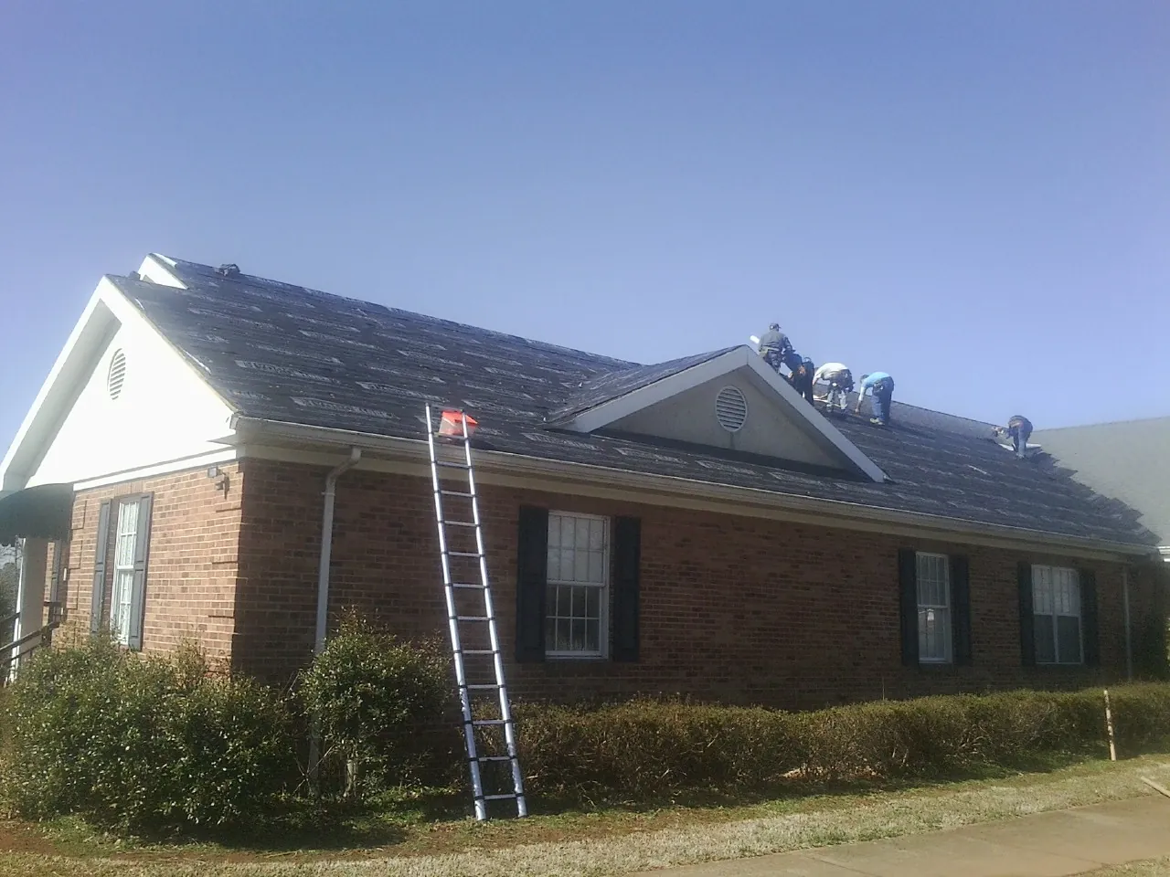 Crew tearing shingles off a brick ranch roof with a ladder set — Emergency Roof Repair work by our crew in East Freetown