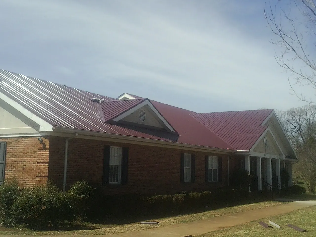 Red metal roof with gabled entries on a long brick building, from a Hail Damage Roof Repair job in East Freetown