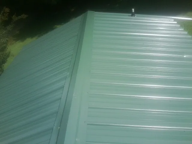 New green metal panels meeting at the ridge of a roof — Flat Roof Repair work by our crew in East Freetown