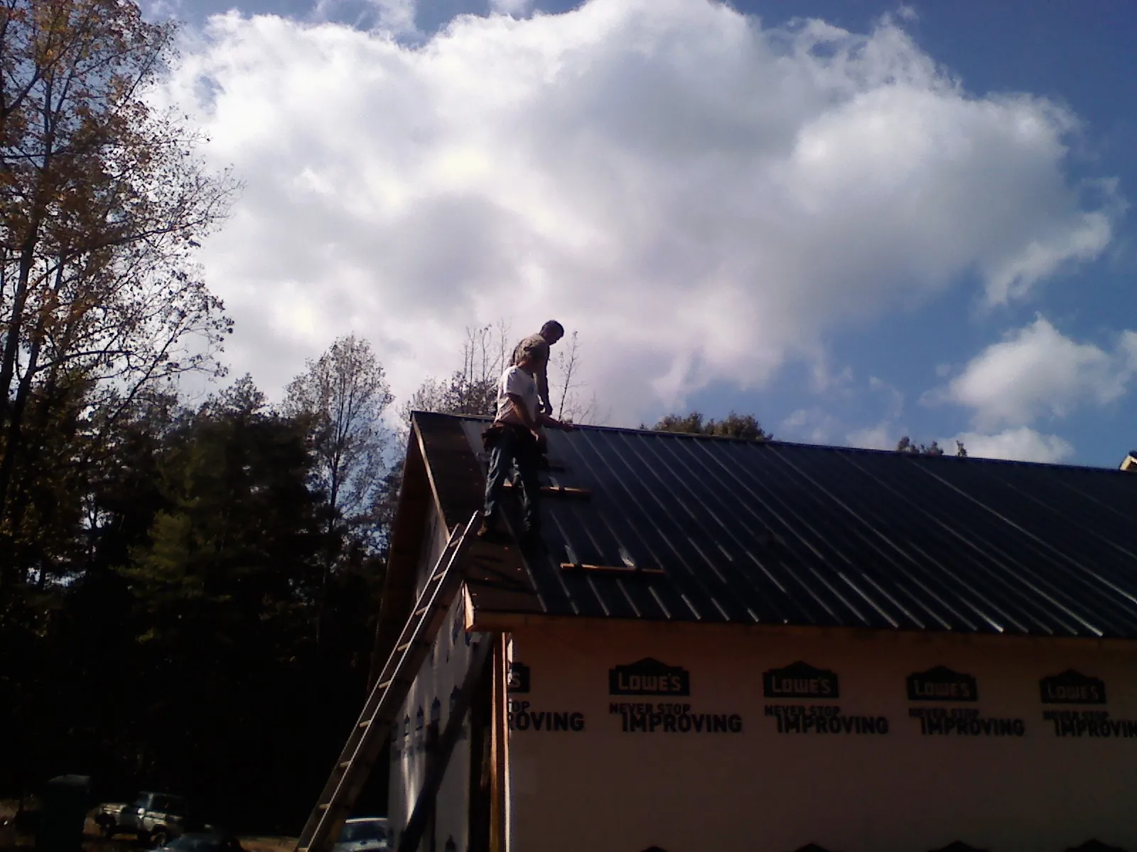 Roofer fastening dark metal panels high against a cloudy sky, from a Roof Inspection job in East Freetown