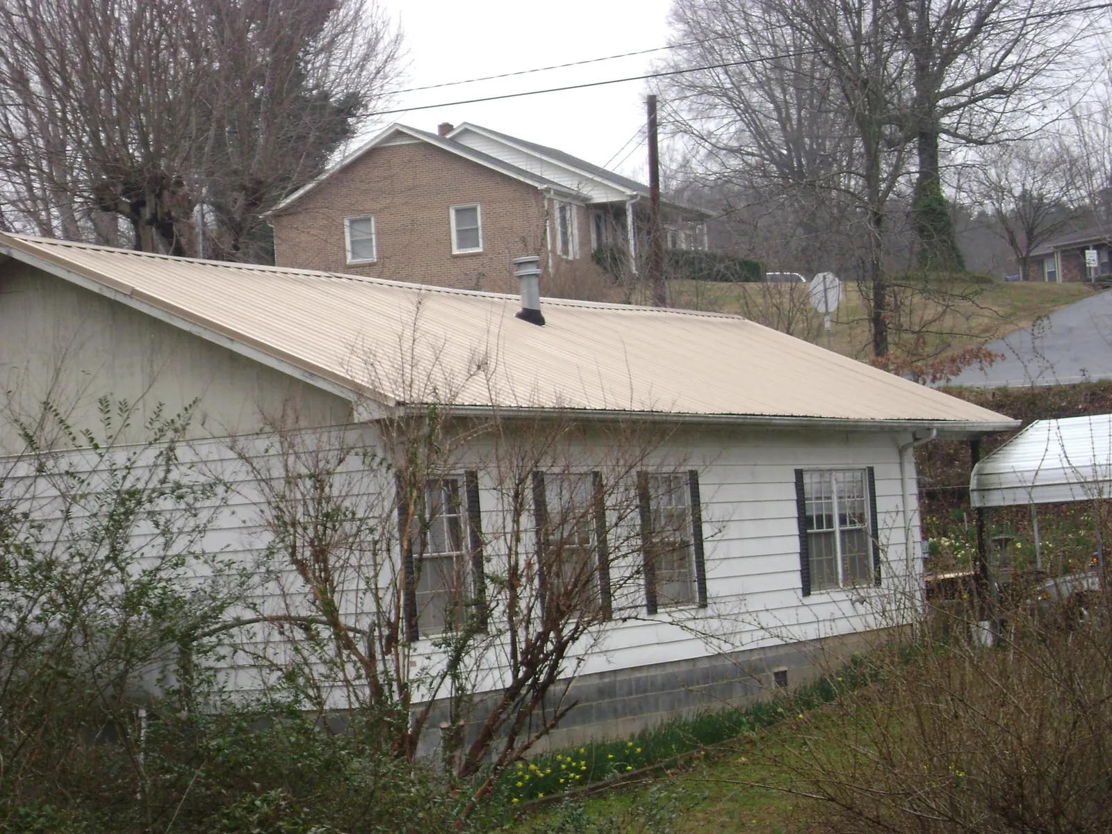 Tan metal roof on a white sided house set into a hillside — Commercial Roofing by Roofing Brothers in East Freetown