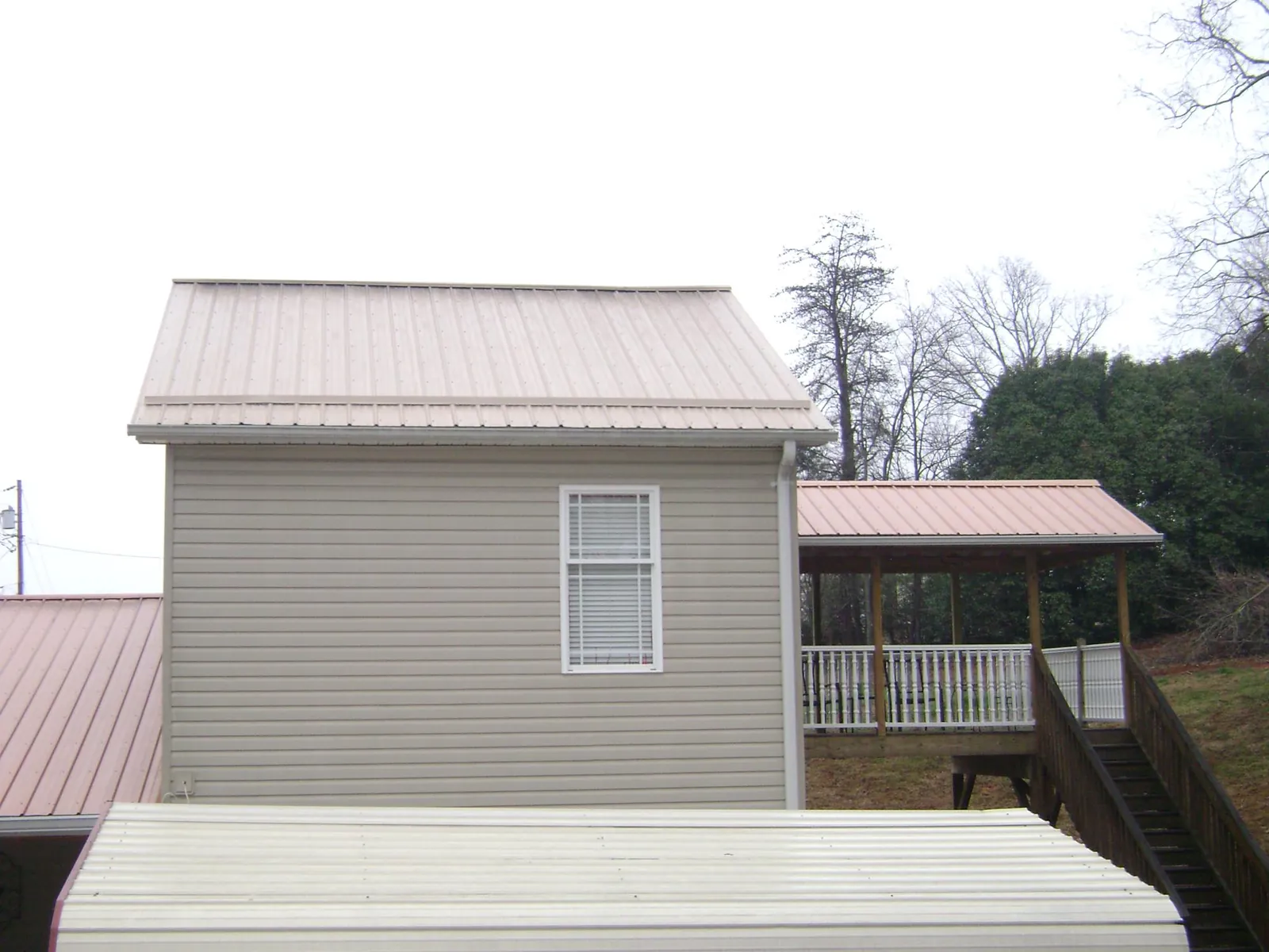 Tan metal roofs on a two story addition and attached porch, from a Roof Replacement job in East Freetown
